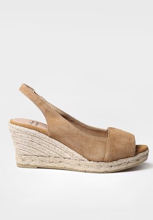 Beige ruskinds kilehælssandal med peep toe, slingback-rem og flettet jute-platformsål, vist i sideprofil på hvid baggrund.