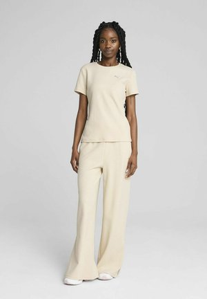 Beige strikket t-shirt med korte ærmer, parret med matchende brede bukser, begge med blød tekstur og minimalistisch design.