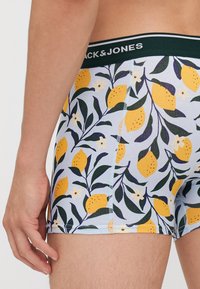 Un caleçon en tissu bleu clair avec un motif de citrons et de fleurs, muni d'une ceinture noire portant la mention "Jack & Jones".