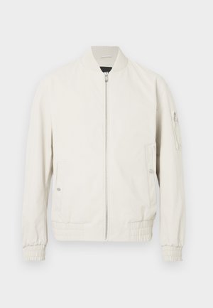 Casaco bomber cinza claro com fecho zipper à frente, gola e punhos canelados, dois bolsos laterais e um bolso com fecho na manga esquerda. Textura suave.