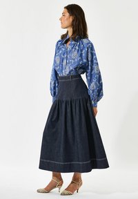 Niebieska bluzka w paisley z bufiastymi rękawami, zestawiona z ciemnogranatową spódnicą o wysokim stanie z marszczonym dołem i białymi przeszyciami.