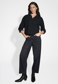 Felpa cropped nera con zip anteriore e cappuccio, abbinata a jeans a vita alta neri con gamba larga e stivaletti neri.
