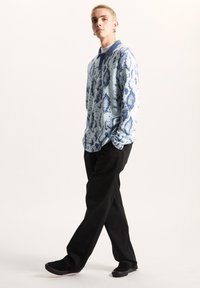 Ljusblå långärmad polo med ett mönster av ormskinn i marinblått, ihop med svarta vida byxor och svarta skor. Slät tygtextur.