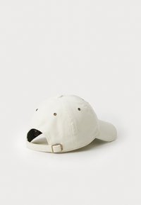 Gorra de béisbol de pana blanca con visera curva, ojales de ventilación y una correa ajustable con un cierre metálico en la parte posterior.