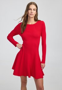 Rode gebreide jurk met lange mouwen, geribbelde textuur, aansluitend lijfje, uitlopende rok en ronde halslijn. Glad materiaal met minimale details.