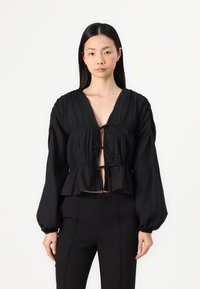Fekete, rövidített blúz mély V-nyakkal, ráncolt ujjakkal és elöl megkötős részlettel. Texturált anyagból készült, laza fazonnal és fodros aljjal.