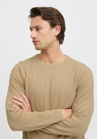 Beige geribbelde trui met lange mouwen en een ronde hals. Zachte textuur, met raglanmouwen en een strakke uitstraling.