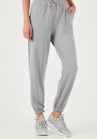Helle graue Jogginghose aus weichem Material mit elastischem Bund, Kordelzug und elastischen Bündchen. Kombiniert mit grauen Sportschuhen.