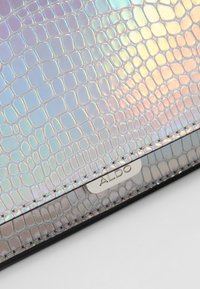 Iridescerende håndtaske med krokodillepræget tekstur, med en sølvmetal "ALDO"-logo på en sort base. Glat finish og reflekterende overflade.