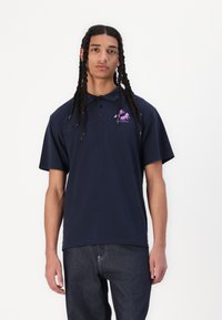 Navy blue polo shirt with a short collar, three black buttons, and a purple horse logo on the left chest. Smooth cotton material, relaxed fit.