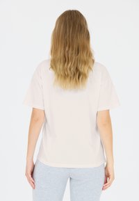 Lichtbeige katoen T-shirt met korte mouwen, relaxed fit en een ronde halslijn. Licht gebogen zoom. Draagt met grijze leggings.
