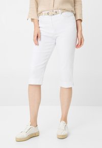 Bermuda shorts bianchi in cotone con taglio dritto, orlo piegato e passanti per cintura, abbinati a scarpe stringate di colore chiaro.
