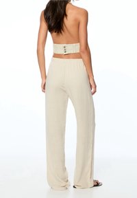Bandeau crop top met knoopdetail aan de achterkant, gecombineerd met lichtbeige, wijde broek in een zachte, gestructureerde stof.