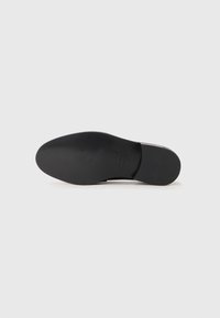 Semelle de chaussure en cuir noir avec finition lisse, montrant le nom de la marque et le numéro de taille sur fond blanc.