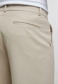 Beige op maat gemaakte broek met een gladde textuur, slim fit en een enkele achterzak met een strakke opening.