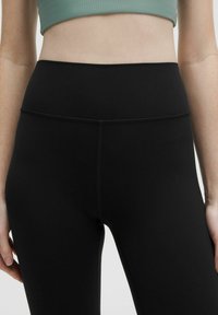 Hochgeschnittene schwarze Leggings aus dehnbarem, mattem Stoff; mit einem nahtlosen Bund und subtilen Nähdetails.