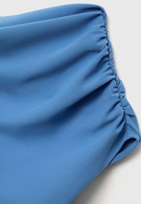 Tissu bleu avec un détail élastique froncé créant des volants le long d'un bord, posé sur un fond clair uni.