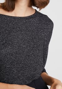 Mörkgrå stickad topp med bred halsringning, texturerat tyg och avslappnad passform. Har långärmar och en mjuk, slät yta.