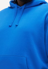 Sweat à capuche bleu en tissu doux, doté d'une grande poche et de cordons ajustables. Texture lisse avec une couleur vive.