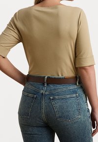 Top beige aderente con scollatura ampia e maniche a tre quarti abbinato a jeans blu strappati a vita alta e una cintura marrone.