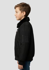 Sort bomberjakke med en blød sort krave, sidelomme og lynlåsdetalje. Har ribstrikkede manchetter og linning. Barn bærer den.