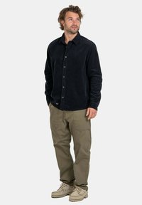 Camicia button-up in corduroy nera, pantaloni cargo color sabbia e scarpe beige. La camicia presenta un colletto standard e maniche lunghe.