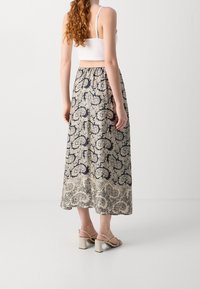 Larga falda fluida con un patrón de paisley en navy y crema. Confeccionada en una tela ligera y de textura suave. Combinada con sandalias de tacón bloque.