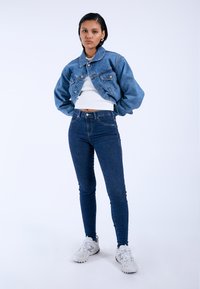 Denim jacket with a cropped design, light blue color, and puffed sleeves, paired with high-waisted dark jeans and white sneakers.