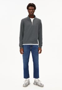 Sudadera gris con cremallera de un cuarto, con un panel superior en contraste. Combinada con jeans azules de pierna recta y zapatillas grises con un patrón.