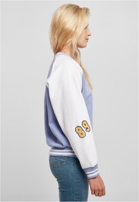 Jasnofioletowy sweatshirt z białymi rękawami, na lewym ramieniu z żółtą cyfrą "89". Żebrowane mankiety i dekolt, wykonany z miękkiego materiału bawełnianego.