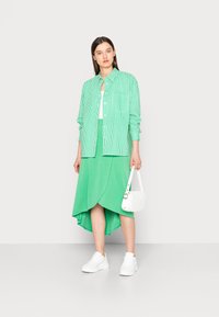 Camisa verde às riscas com um bolso, combinada com uma saia assimétrica verde lisa, ténis brancos e uma mala branca acolchoada.