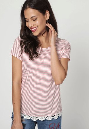 Camiseta de rayas rojas y blancas, de manga corta, fabricada en tejido suave, con un borde decorativo de encaje blanco en el dobladillo. Llevada con jeans azules.