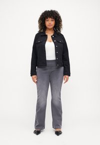 Črna jeans jakna z gumbom, sivo široke hlače iz mehkega materiala in črne čevlje z ostro konico ter zaponkami.