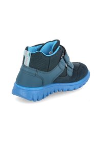 Dunkelgrüne und blaue Kinderknöchelstiefel mit zwei Klettverschlüssen, strukturiertem Stoffoberteil und einer klobigen blauen Gummisohle.