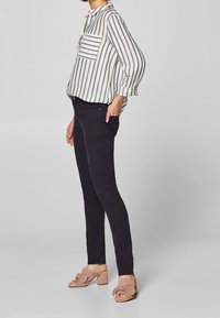 Camisa de rayas de manga larga con un bolsillo en el pecho, combinada con pantalones negros ajustados y sandalias de tacón color rosa claro con un diseño de nudo.