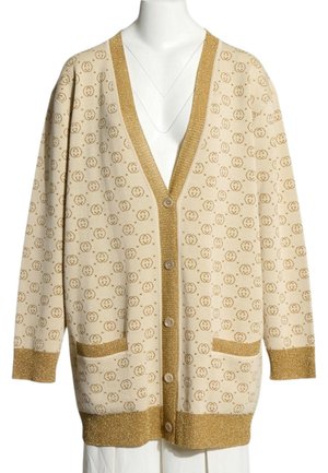 Beige lange cardigan met kleine cirkelvormige patronen van logo's, gouden bies op manchetten, zakken, knopenbies en zoom, tentoongesteld op een paspop.