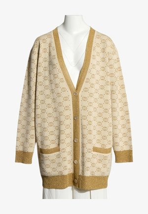 Beigefarbener langer Cardigan mit kleinen kreisförmigen Musterlogos, goldfarbener Besatz an Bündchen, Taschen, Knopfleiste und Saum, präsentiert auf einer Schaufensterpuppe.