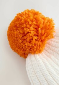 Knit hat featuring a large, fluffy orange pom-pom atop a white ribbed fabric, showcasing a soft texture and rounded shape.