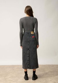 Czarna spódnica dżinsowa z tylnym rozcięciem, wysoki stan i kieszeniami. Połączona z dopasowanym szarym swetrem z prążkowanej tkaniny oraz czarnymi butami na grubych podeszwach.