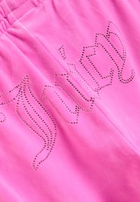 Rosa Velours-Hose mit elastischem Bund, auf dem "Juicy" in kleinen, glänzenden Strasssteinen über den Stoff verteilt geschrieben steht.