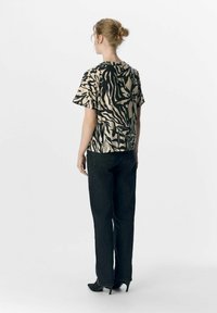 Kortærmet top med zebra-print i beige og sort, parret med højtaljet sorte jeans. Sættet har en løs pasform og struktureret design.