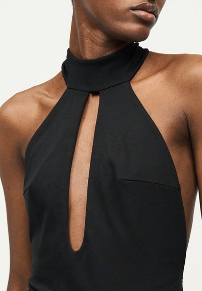 Gros plan sur une personne portant un haut noir sans manches à col montant avec une découpe en forme de trou de serrure à l'avant.