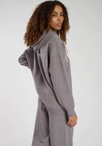 Grauer übergroßer Hoodie mit geripptem Saum und Bündchen, der eine Kapuze hat. Der Stoff wirkt weich mit einer dezenten Textur.