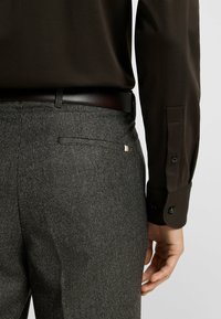 Bruine lange mouwen shirt gecombineerd met grijze houndstooth broek. De broek heeft een elegante achterzak met een klein accentdetail.
