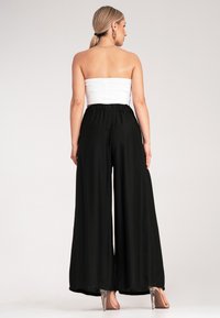 Czarne szerokie spodnie wykonane z lekkiego materiału, z elastycznym paskiem w talii, zestawione z dopasowanym białym topem bez ramiączek.