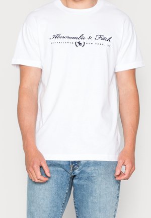 Biała bawełniana koszulka z krótkim rękawem, z granatowym logo "Abercrombie & Fitch" z emblematem powyżej. Klasyczny okrągły dekolt, luźny krój.