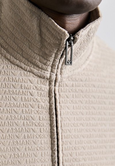 Bežna jakna na zatvaranje sa žicom s utisnutim uzorkom "Emporio Armani", koja ima visoki ovratnik i srebrne dijelove sa zatvaračem, izrađena od mekog teksturiranog materijala.