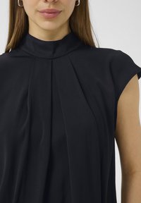 Blusa nera con colletto alto, maniche a capo e pieghe frontali. Tessuto morbido con un design fluido e drappeggiato per una vestibilità rilassata.