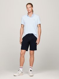 Lyseblå poloskjorte med korte ermer, mørk marineblå shorts, hvite sneakers med svarte detaljer, og stripete hvite sokker. Pen, avslappet passform.