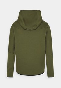 Olivgrön hoodie med stor huva, slät textur, böjda axelsömmar och svarta kantdetaljer. Bakifrån, med långa ärmar.
